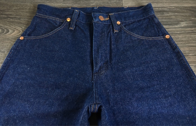 Puede incluir: Un par de pantalones vaqueros de mezclilla azul oscuro con un estilo cl&aacute;sico de cinco bolsillos. Los pantalones tienen una cintura alta y una pierna recta.