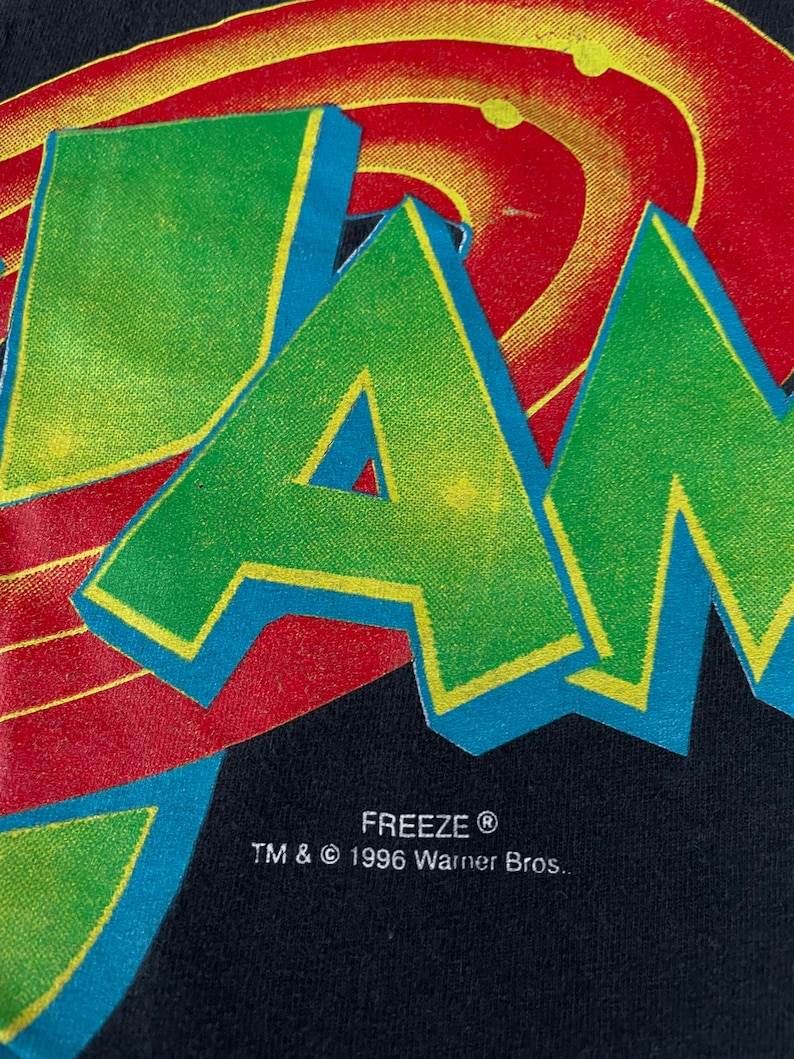 May include: Black t-shirt featuring a green, yellow and blue "JAM" graphic with a red and yellow swirl design behind it. The text "FREEZE&reg; TM & &copy; 1996 Warner Bros." is printed below the graphic.