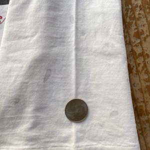 K&ouml;nnte beinhalten: Wei&szlig;es T-Shirt mit einem schwachen Fleck und einer US-Viertel-Dollar-M&uuml;nze als Gr&ouml;&szlig;envergleich.