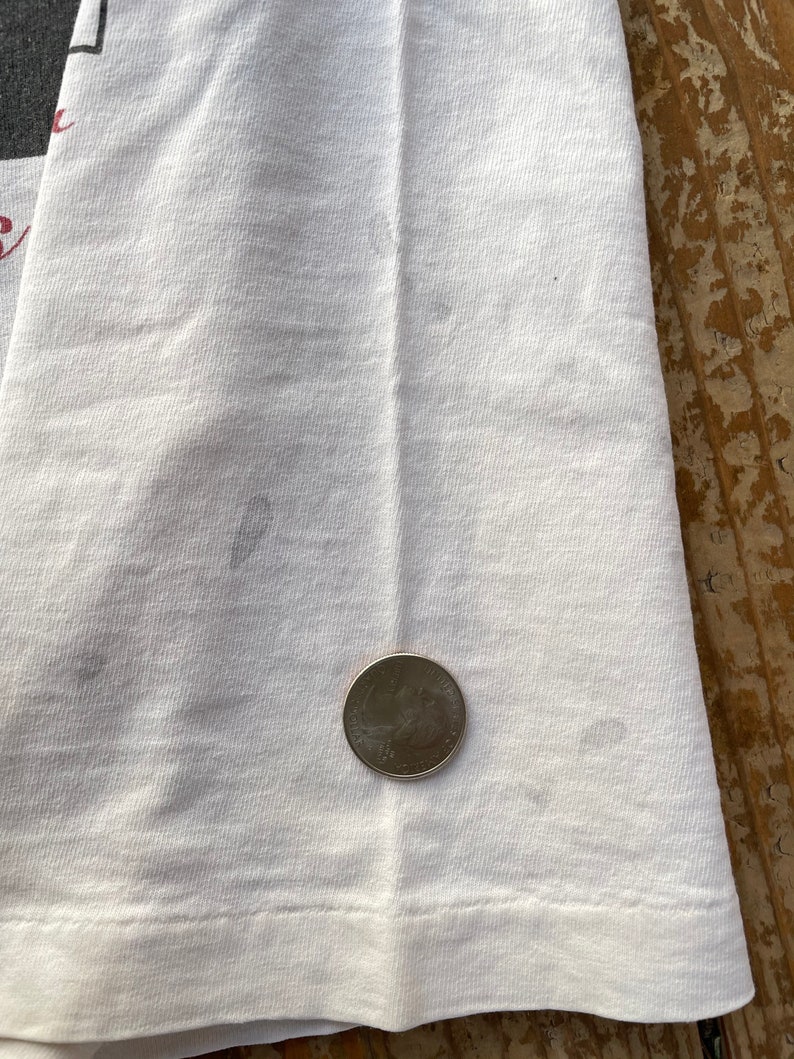 K&ouml;nnte beinhalten: Wei&szlig;es T-Shirt mit einem schwachen Fleck und einer US-Viertel-Dollar-M&uuml;nze als Gr&ouml;&szlig;envergleich.