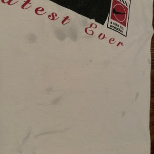 K&ouml;nnte beinhalten: Wei&szlig;es T-Shirt mit einer schwarz-wei&szlig;en Grafik einer Person mit dem Text "greatest ever" und einem rot-wei&szlig;en Nike-Logo mit dem Text "a nike inc. production".