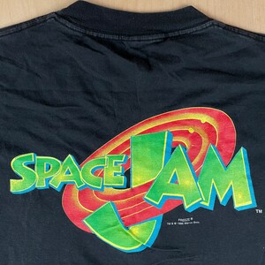 May include: Black t-shirt with a green and red Space Jam logo featuring the words "Space Jam" and the Warner Bros. "Freeze" logo.