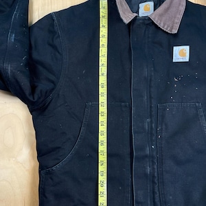 May include: Black Carhartt jacket with a brown corduroy collar. The jacket has two large front pockets and a Carhartt logo patch. A measuring tape shows the jacket is approximately 24 inches long.
