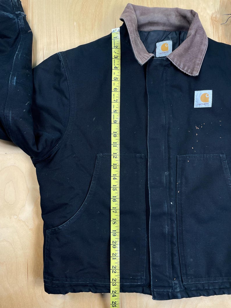 May include: Black Carhartt jacket with a brown corduroy collar. The jacket has two large front pockets and a Carhartt logo patch. A measuring tape shows the jacket is approximately 24 inches long.