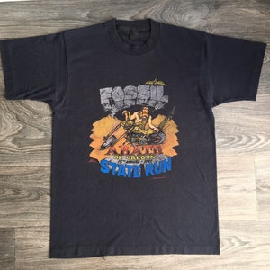 May include: Black t-shirt with a graphic of a cartoon caveman riding a motorcycle with the text "Fossil Fuel Abate of Oregon 15th Annual 1992 State Run".