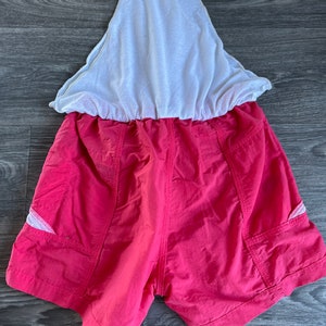 May include: Pink athletic shorts with white mesh lining and side pockets. The shorts have a drawstring waist.