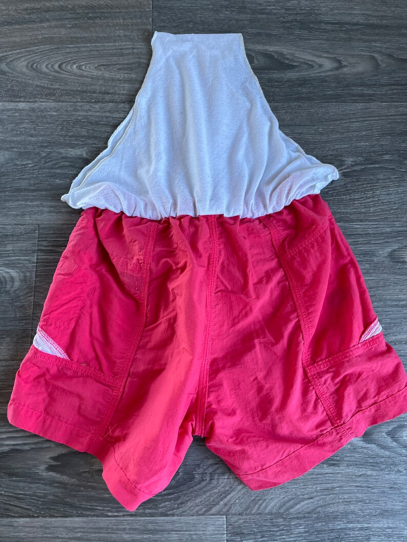 May include: Pink athletic shorts with white mesh lining and side pockets. The shorts have a drawstring waist.