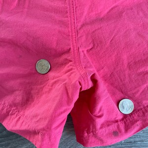 May include: Close-up of a pair of pink shorts with two US quarters placed on the fabric. The shorts have a seam down the center back.