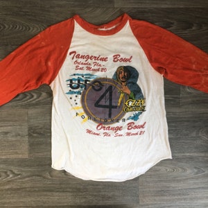 May include: A white and orange baseball style t-shirt with a graphic of a concert featuring Ozzy Osbourne, UFO, Foreigner, and a band called "Up 4". The text reads "Tangerine Bowl, Orlando, Fla. - Sat. March 20" and "Orange Bowl, Miami, Fla. - Sun. March 21".