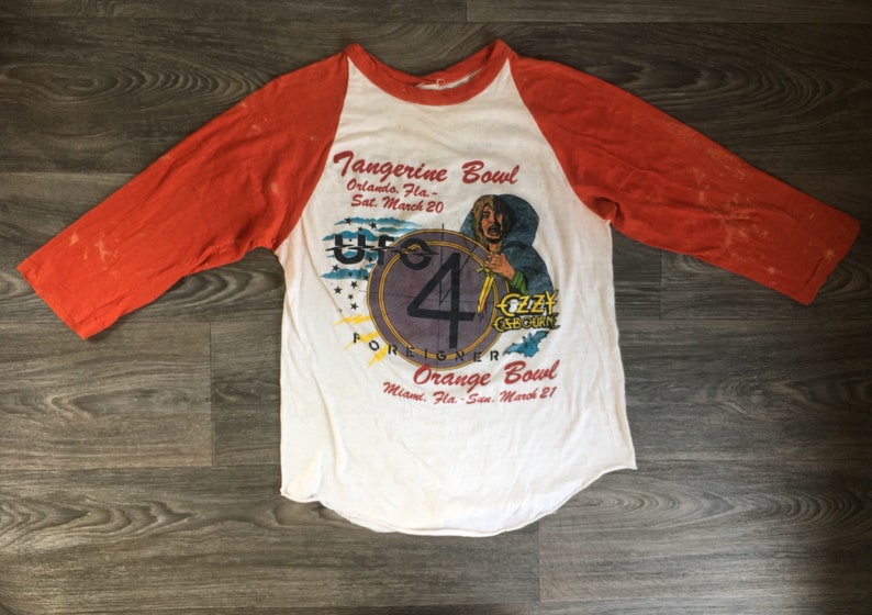 May include: A white and orange baseball style t-shirt with a graphic of a concert featuring Ozzy Osbourne, UFO, Foreigner, and a band called "Up 4". The text reads "Tangerine Bowl, Orlando, Fla. - Sat. March 20" and "Orange Bowl, Miami, Fla. - Sun. March 21".
