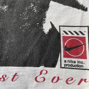 K&ouml;nnte beinhalten: Wei&szlig;es T-Shirt mit einem schwarz-wei&szlig;en Grafikdruck eines Personenkopfes. Die Grafik ist im Used-Look gehalten. Das Shirt hat au&szlig;erdem ein rotes und wei&szlig;es Nike-Logo mit dem Text "a nike inc. production" darunter. Der Text "best ever" ist in Rot am unteren Rand des Shirts aufgedruckt.