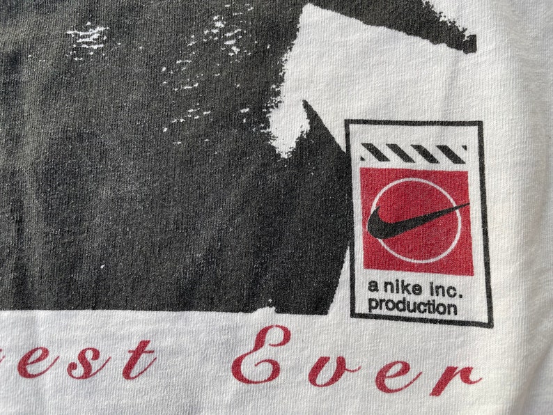 K&ouml;nnte beinhalten: Wei&szlig;es T-Shirt mit einem schwarz-wei&szlig;en Grafikdruck eines Personenkopfes. Die Grafik ist im Used-Look gehalten. Das Shirt hat au&szlig;erdem ein rotes und wei&szlig;es Nike-Logo mit dem Text "a nike inc. production" darunter. Der Text "best ever" ist in Rot am unteren Rand des Shirts aufgedruckt.