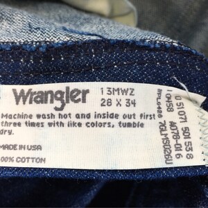 Puede incluir: Etiqueta de cuidado blanca con texto negro para jeans Wrangler. La etiqueta incluye la talla 28 x 34, el n&uacute;mero de estilo 13MWZ y las instrucciones de lavado. La etiqueta tambi&eacute;n indica "Hecho en EE. UU." y "100 % algod&oacute;n".