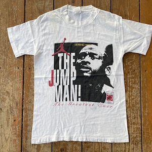 K&ouml;nnte beinhalten: Wei&szlig;es T-Shirt mit einer schwarz-wei&szlig;en Grafik von Michael Jordan, dem Text "The Jumpman" und den Worten "The Greatest Ever".