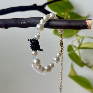 May include: A white pearl bracelet with a black beaded bird charm. The bracelet has a gold chain extender.
