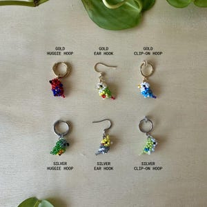 May include: Six pairs of beaded bird earrings in gold and silver. The earrings are available in three styles: huggie hoop, ear hook, and clip-on hoop.
