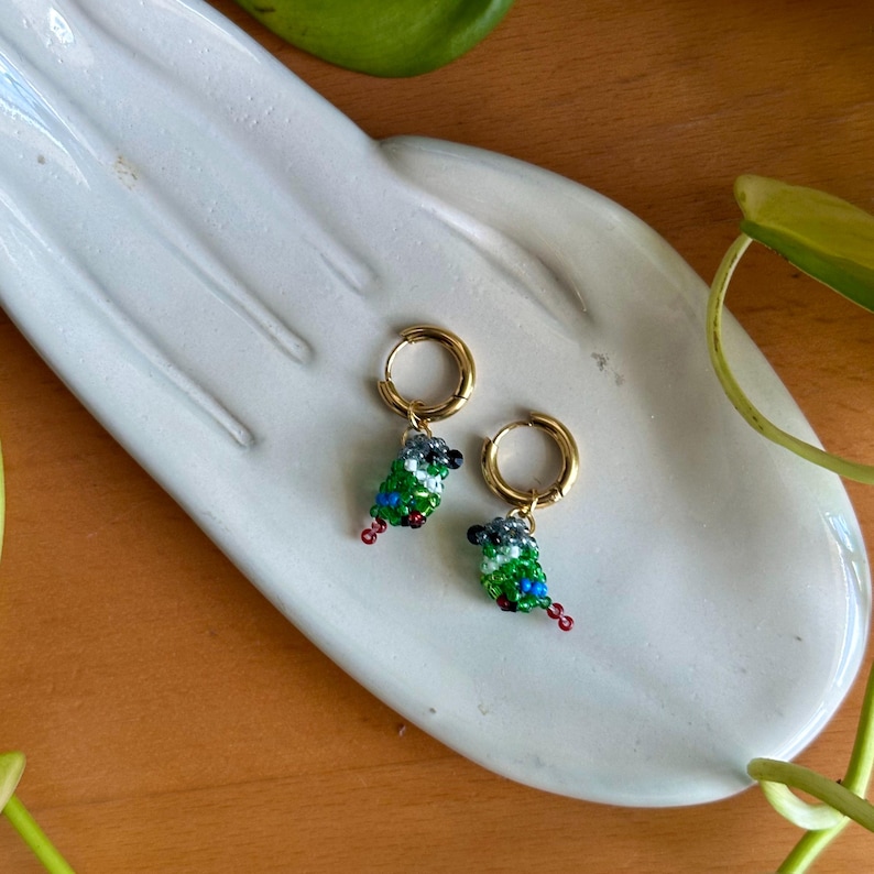 May include: A pair of gold hoop earrings with small green, blue, and black beaded bird charms hanging from them.