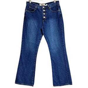 May include: Dark blue denim jeans with a button fly and a flared leg. The jeans have a classic five-pocket design and are hanging on a hanger. The denim has a medium wash with some fading.