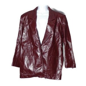 May include: A burgundy leather jacket with a classic blazer style, featuring a single-breasted closure, long sleeves, and two pockets.
