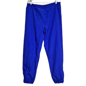 May include: Bright blue athletic pants hanging on a white hanger. The pants are made of a lightweight material and have an elastic waistband and cuffs. The pants are a solid color and appear to be in good condition.