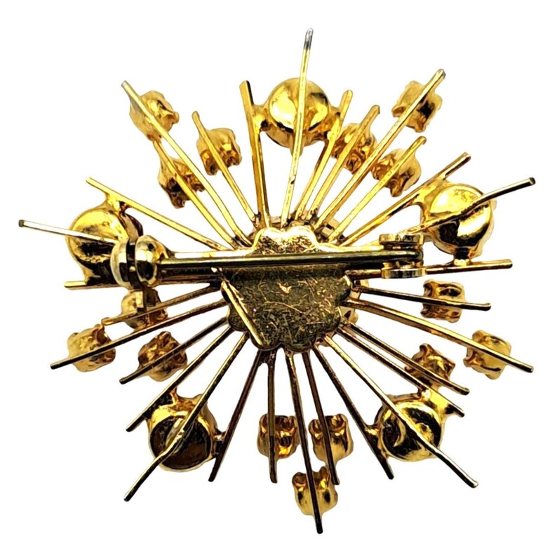 Puede incluir: Broche dorado con dise&ntilde;o de estrella. El broche presenta un pasador y cierre central, con l&iacute;neas radiales y peque&ntilde;os acentos redondos de color dorado. La parte posterior del broche es visible, mostrando el mecanismo del pasador.