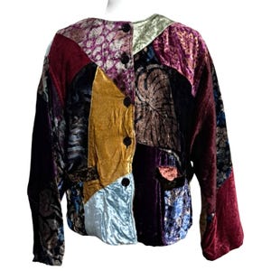 May include: A patchwork jacket with a variety of jewel-toned velvet fabrics. The jacket features a round collar, long sleeves, and black buttons down the front. The design includes shades of burgundy, gold, purple, and teal.