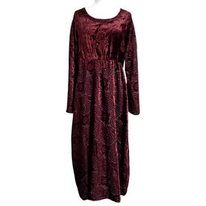 May include: A burgundy velvet dress with long sleeves and a round neckline. The dress features a floral pattern on the bodice and a circular design throughout the skirt. The dress has a cinched waist and a flowing, floor-length hemline.