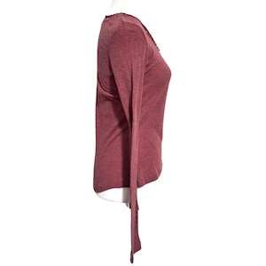 May include: A long-sleeved, maroon-colored shirt with a V-neck and a decorative trim along the neckline. The shirt is made of a soft, lightweight material and has a slim fit. The sleeves are long and end in a simple cuff.