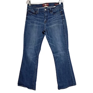 May include: Blue denim jeans with a bootcut leg. The jeans have a classic five-pocket design, a button and zipper closure, and a Lucky Brand label on the back pocket. The jeans are hanging on a white hanger.