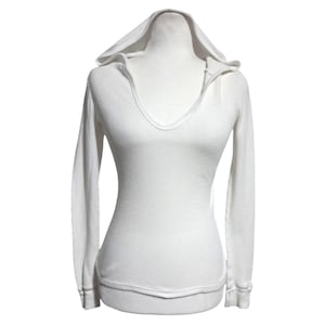 May include: White waffle-knit hoodie with a deep V-neck. The long-sleeved top features a fitted silhouette and a hood. The cuffs and hem have a ribbed texture. The garment is displayed on a mannequin.