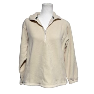 May include: A cream-colored fleece pullover with a quarter-zip closure and long sleeves. The pullover has a small logo on the bottom right side.