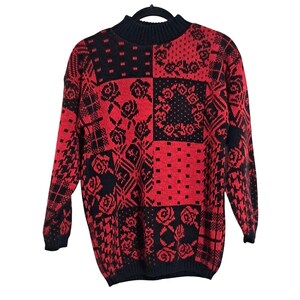 May include: A red and black patchwork sweater with a mock turtleneck. The sweater features various geometric and floral patterns, including roses and polka dots. The long-sleeved sweater is hanging on a black hanger.