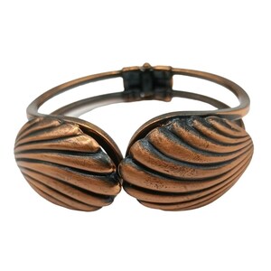 May include: A copper-toned bangle bracelet with a shell design. The bracelet is made of two overlapping shells with a textured surface.