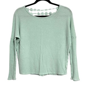 May include: A light green waffle knit long-sleeve shirt with a floral lace detail across the upper back. The shirt is hanging on a black hanger. The sleeves have a ribbed cuff.
