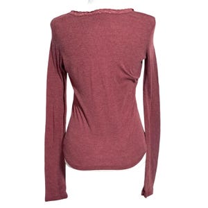 May include: A long-sleeved, maroon-colored shirt with a scoop neck and lace trim. The shirt has a fitted silhouette and is made of a soft, textured fabric. The back of the shirt is visible in the image.