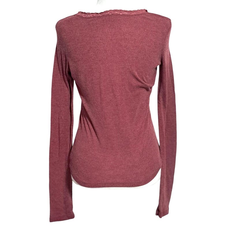 May include: A long-sleeved, maroon-colored shirt with a scoop neck and lace trim. The shirt has a fitted silhouette and is made of a soft, textured fabric. The back of the shirt is visible in the image.