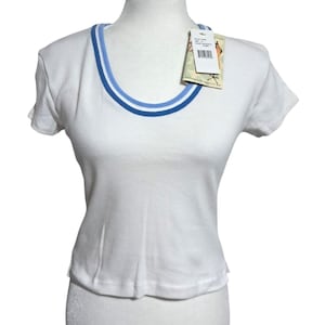 May include: White short-sleeve t-shirt with a scoop neck. The neckline is trimmed with a light blue and navy blue stripe. A product tag is attached to the shirt. The shirt is displayed on a mannequin.