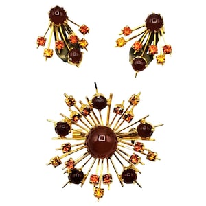 Puede incluir: Un conjunto de joyas vintage que incluye un broche y pendientes a juego. El conjunto tiene un engaste de metal dorado con piedras grandes, redondas, de color marr&oacute;n rojizo y piedras de acento naranja-amarillo m&aacute;s peque&ntilde;as. Los pendientes tienen un dise&ntilde;o de racimo.