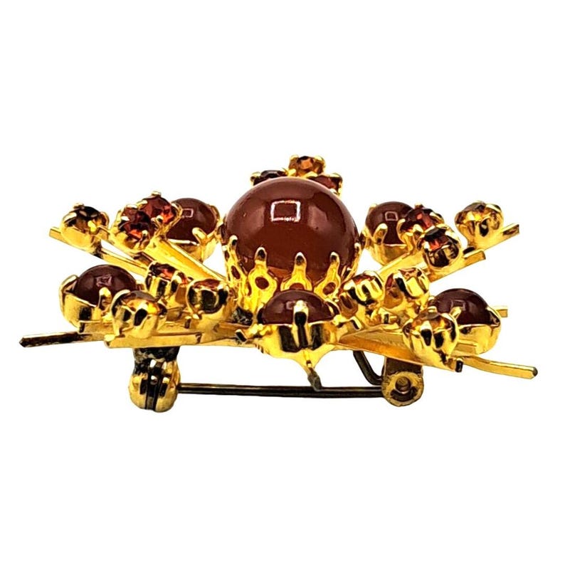 Puede incluir: Broche dorado con una piedra central grande, redonda y marr&oacute;n, rodeada de piedras marrones m&aacute;s peque&ntilde;as y detalles dorados. El broche tiene un cierre de alfiler y est&aacute; dise&ntilde;ado en un estilo floral o abstracto.