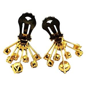 Puede incluir: Un par de pendientes vintage de clip. Cada pendiente presenta un clip negro y un dise&ntilde;o de metal dorado. El dise&ntilde;o dorado tiene m&uacute;ltiples brazos radiantes, cada uno de los cuales termina en una peque&ntilde;a piedra preciosa amarilla redonda.