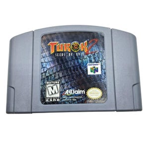 May include: A gray Nintendo 64 video game cartridge for Turok 2: Seeds of Evil. The label features the game's title in red and yellow, a textured background, and the Nintendo logo. The cartridge is rated "M" for Mature.