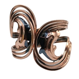 May include: A copper bracelet with a swirling design and two stylized dolphin shapes. The dolphins are outlined in copper and filled with black enamel.