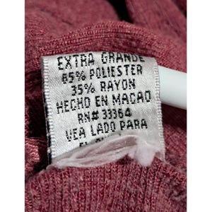May include: Close-up of a tag with the words "EXTRA GRANDE" and fabric composition details: 65% POLIESTER, 35% RAYON. The tag also includes "HECHO EN MACAO" and "RN# 33364". The tag is attached to a maroon fabric.