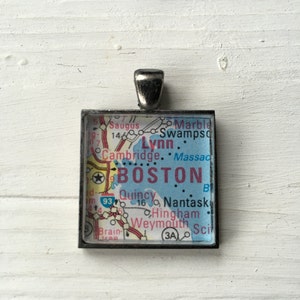 May include: A silver charm necklace featuring a map of Boston, Massachusetts. The map is printed on a blue background with red and black lines. The charm is surrounded by a silver frame.