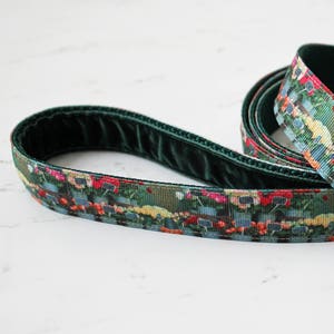 Puede incluir: Una correa de perro verde con estampado floral y un clip plateado. La correa está hecha de dos capas de tela, una con textura de terciopelo y la otra con estampado floral.