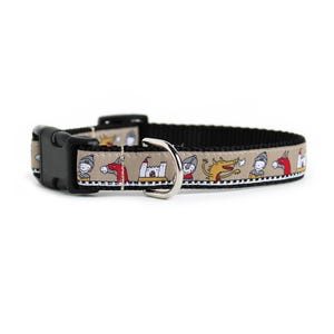 Puede incluir: Un collar para mascotas de color beige con un patrón repetitivo de caballeros, caballos, castillos y dragones amarillos. El collar incluye una hebilla de plástico negra, una anilla en D de metal plateado y una correa de nailon negra.