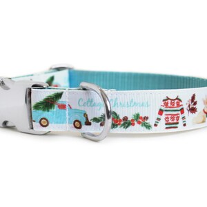 May include: A white dog collar with a festive Christmas design. The collar features a light blue interior and a repeating pattern of a blue truck carrying a Christmas tree, a holiday sweater, and a bunny. The text "Cottage Christmas" is also visible.