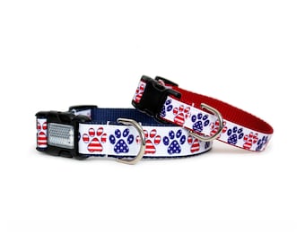 Puede incluir: Dos collares para perros con fondo blanco y huellas de patas rojas y azules. Las huellas de patas están diseñadas para parecerse a la bandera estadounidense. Un collar es rojo y el otro es azul marino.