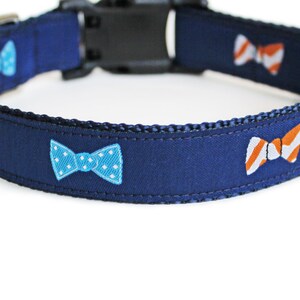 May include: A navy blue dog collar with a repeating pattern of colorful bow ties. The bow ties are green, blue with white polka dots, and orange and white striped.