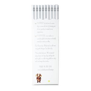 May include: A white rectangular product box with a gray striped design at the top. The box features text about the product's inspiration, handmade nature, and care instructions. A dachshund illustration is at the bottom.